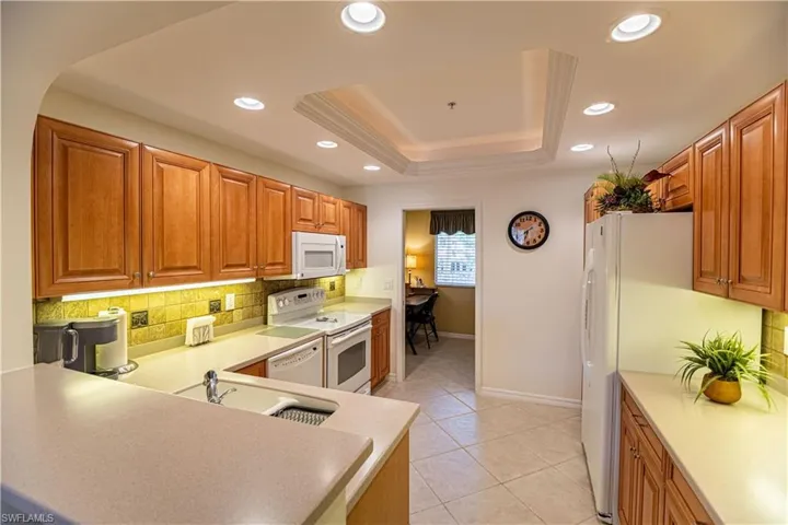Kitchen with backsplash, a raised ceiling, white appliances, brown cabinets, and recessed lighting