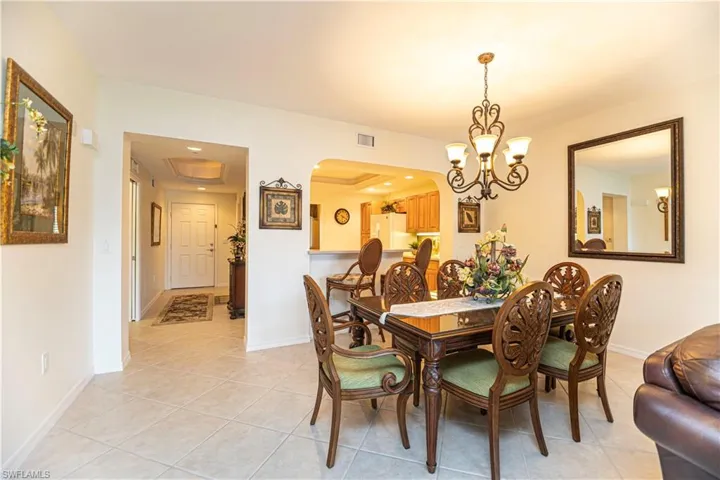 Dining room with light tile patterned floors, arched walkways, a chandelier, a raised ceiling, and recessed lighting