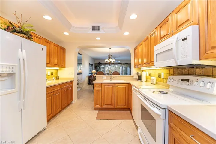 Kitchen featuring white appliances, a chandelier, a tray ceiling, recessed lighting, and backsplash