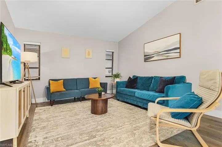 Living room featuring baseboards, visible vents, wood finished floors, and lofted ceiling