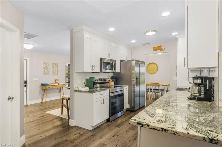 Kitchen with appliances with stainless steel finishes, wood finished floors, white cabinets, and light stone countertops