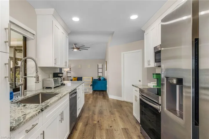 Kitchen with a ceiling fan, wood finished floors, white cabinetry, a sink, and appliances with stainless steel finishes