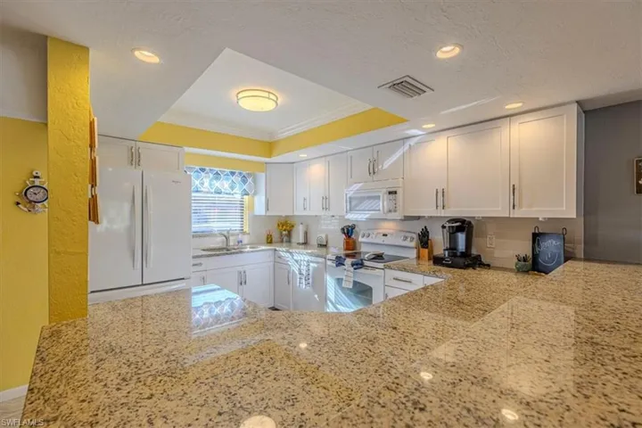 Kitchen with light stone countertops, white appliances, white cabinets, a tray ceiling, and backsplash