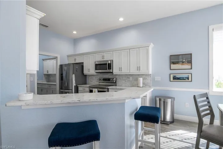 View of kitchen from open great room featuring a breakfast bar, and recessed lighting. Opening to left leads to utility room with cabinets, newer Maytag washer and dryer, quartz counters and door to 2 car garage.
