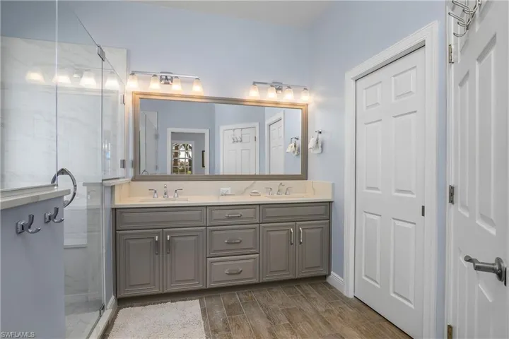 Master bath with walk-in frameless shower, dual sinks, new lighting. One closed door leads to water closet, the other to a linen closet.