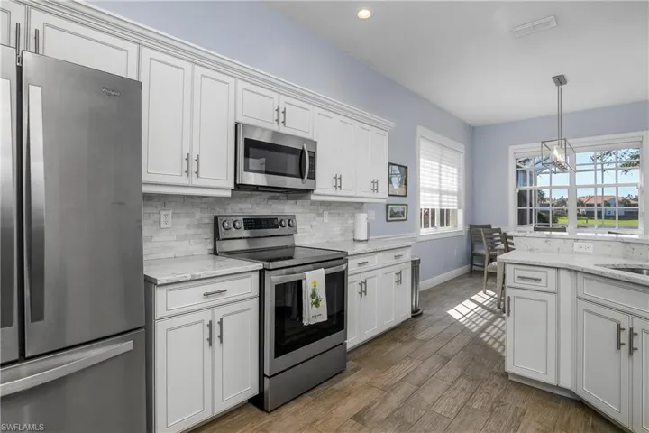 Kitchen featuring stainless steel appliances, white custom cabinetry, stone backsplash, quartz countertops. New lighting fixtures...dining area with window view of lanai seats 6.