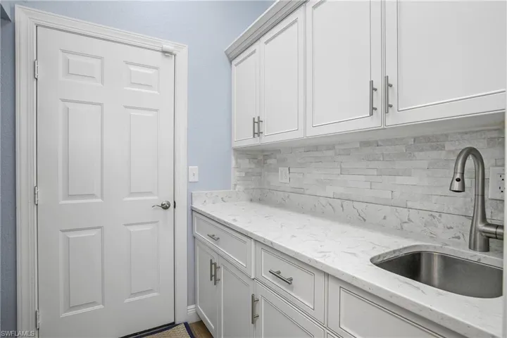 Utility room with plenty of storage space, quartz counters, stone backsplash and laundry tub. Washer and dryer are on opposite wall.
