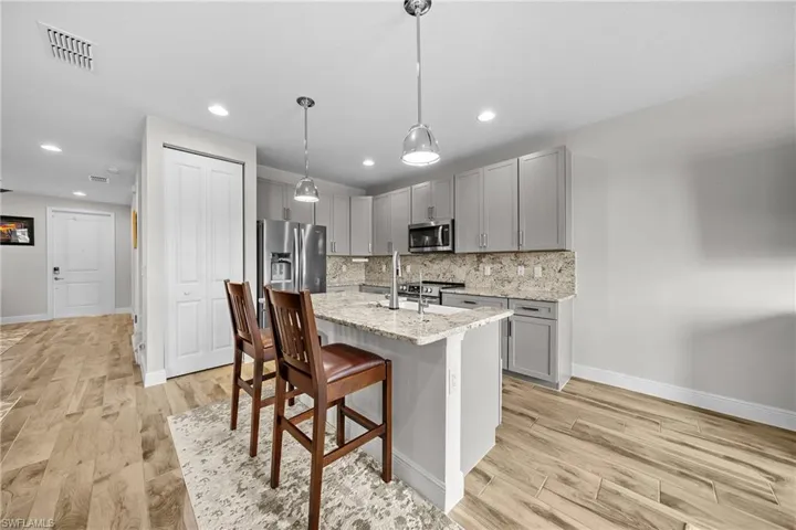 Kitchen featuring gray cabinets, light stone counters, light wood-style flooring, a kitchen bar, and recessed lighting