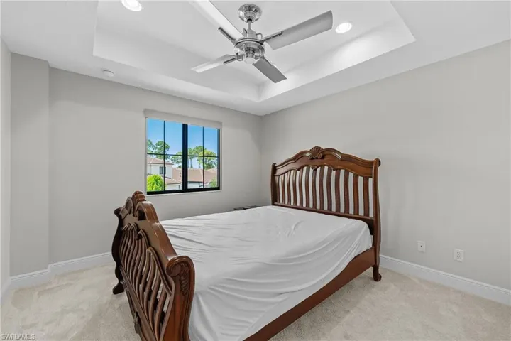 Bedroom featuring a raised ceiling, light colored carpet, and a ceiling fan
