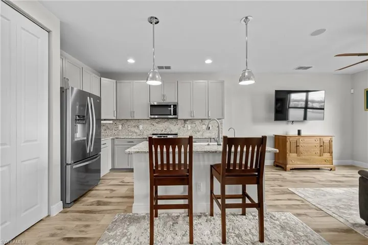Kitchen with stainless steel appliances, backsplash, light stone countertops, decorative light fixtures, and a kitchen bar