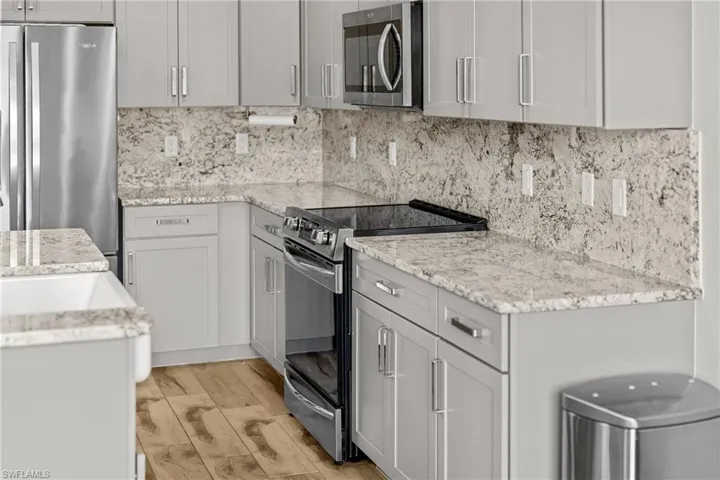 Kitchen with appliances with stainless steel finishes, light stone countertops, tasteful backsplash, and light wood-type flooring