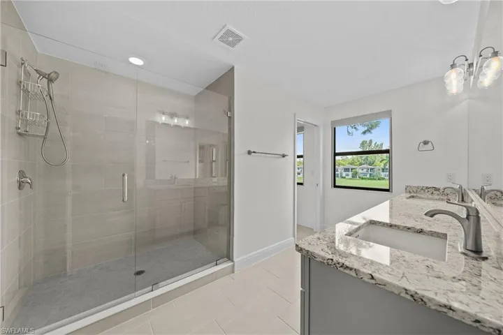 Full bath featuring double vanity, a shower stall, light tile patterned floors, and recessed lighting
