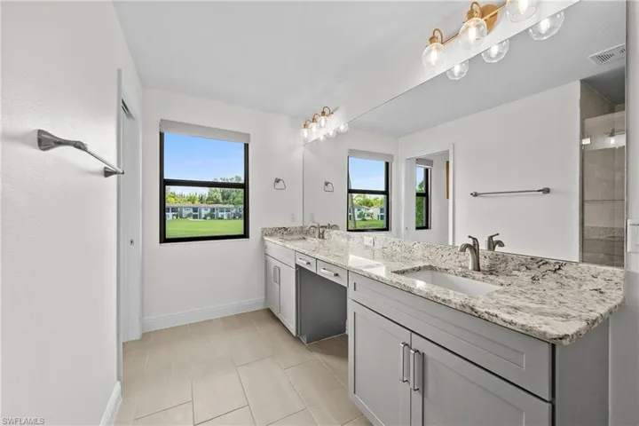 Bathroom with double vanity, light tile patterned flooring, and tiled shower