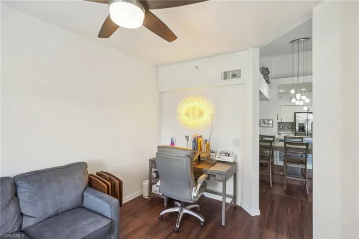 Office space with ceiling fan with notable chandelier, visible vents, wood finished floors, and baseboards