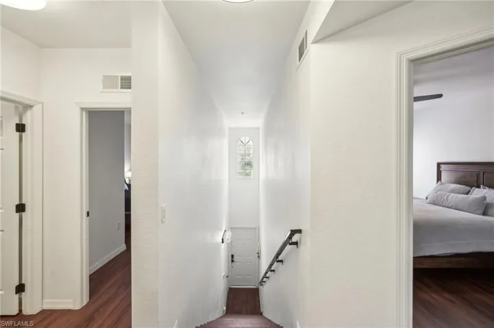 Hallway with wood finished floors, an upstairs landing, and visible vents