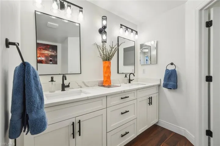 Full bath featuring double vanity, wood finished floors, baseboards, and a sink