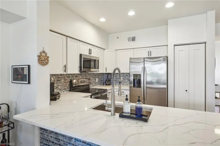 Kitchen with decorative backsplash, white cabinets, visible vents, light stone countertops, and appliances with stainless steel finishes