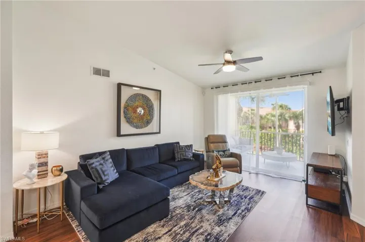 Living room featuring visible vents, vaulted ceiling, a ceiling fan, and wood finished floors