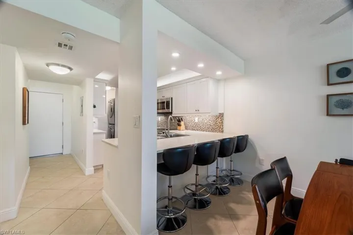 Kitchen with decorative backsplash, light tile patterned floors, a kitchen breakfast bar, white cabinets, and stacked washer and clothes dryer