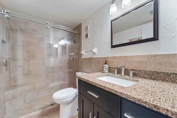 Bathroom with a textured wall, a shower stall, vanity, tile walls, and decorative backsplash