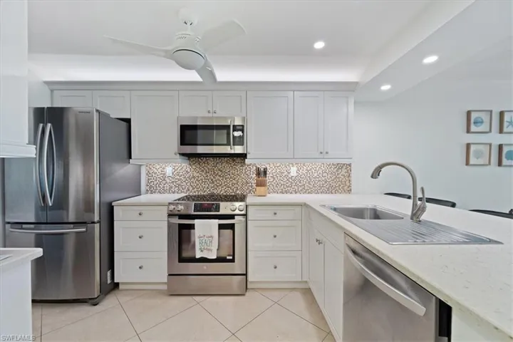 Kitchen featuring stainless steel appliances, tasteful backsplash, light stone counters, white cabinets, and recessed lighting