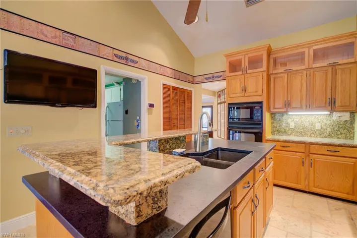 Kitchen with black appliances, dark stone countertops, tasteful backsplash, a center island with sink, and high vaulted ceiling