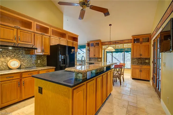 Kitchen featuring brown cabinetry, tasteful backsplash, black fridge with ice dispenser, dark stone countertops, and stone tile floors