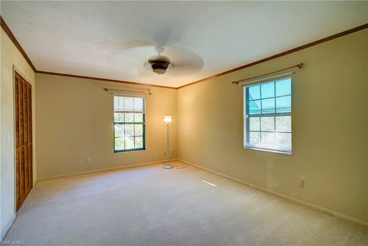 Unfurnished bedroom with a closet, light carpet, multiple windows, a ceiling fan, and ornamental molding