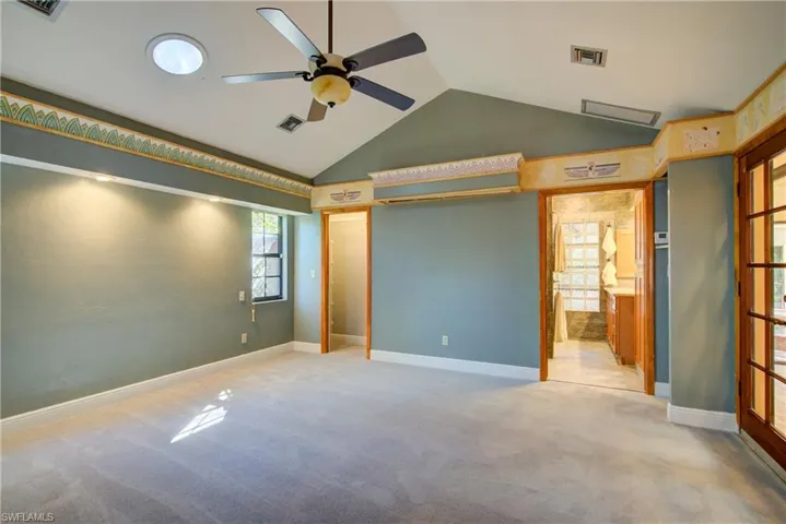 Unfurnished bedroom with light colored carpet, ceiling fan, vaulted ceiling, and connected bathroom