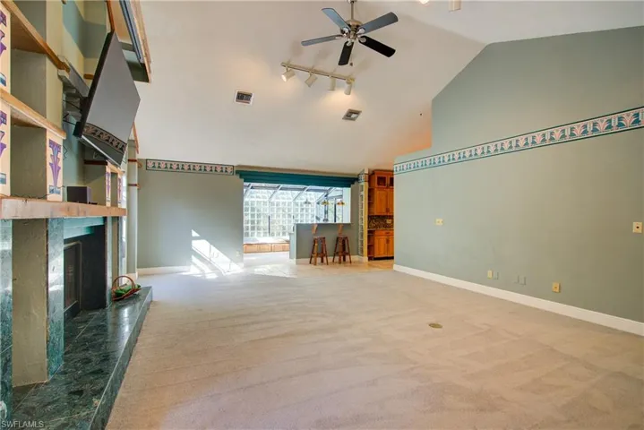 Unfurnished living room with high vaulted ceiling, light colored carpet, rail lighting, a ceiling fan, and a high end fireplace