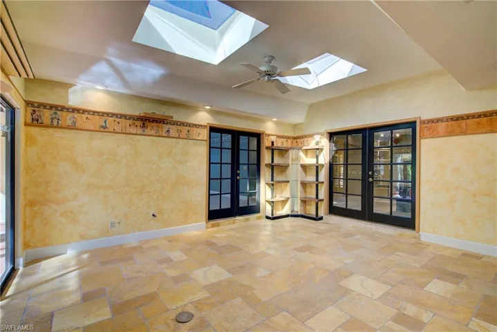 Spare room featuring french doors, stone tile flooring, a skylight, and a ceiling fan