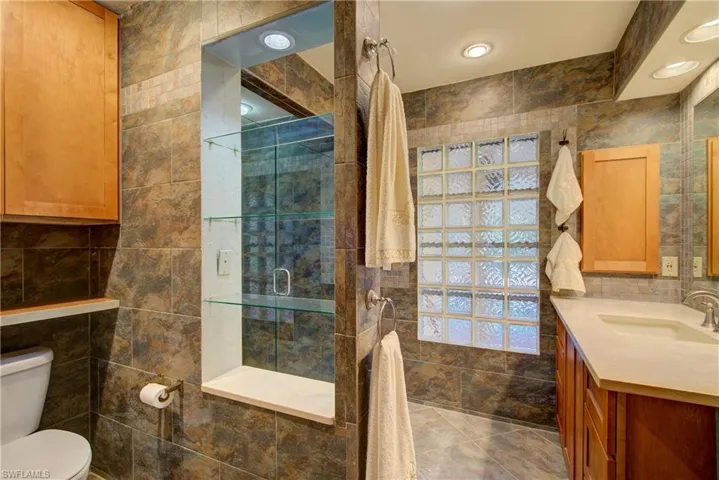 Full bath with tile walls, a stall shower, vanity, and recessed lighting