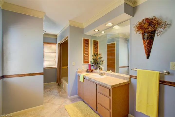 Full bathroom featuring crown molding, vanity, a garden tub, and light tile patterned floors