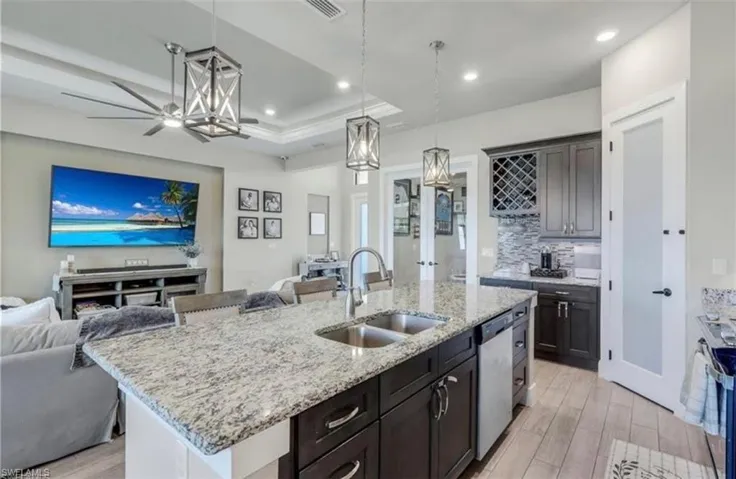 Kitchen with open floor plan, hanging light fixtures, light wood-style flooring, light stone countertops, and a kitchen island with sink