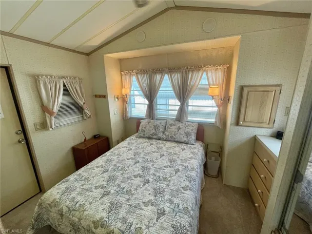 Carpeted bedroom featuring lofted ceiling and wallpapered walls