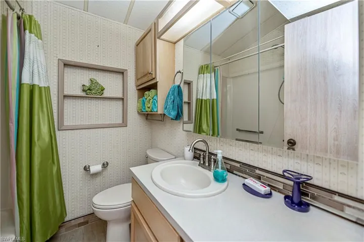 Bathroom featuring wallpapered walls, toilet, a shower with shower curtain, and vanity
