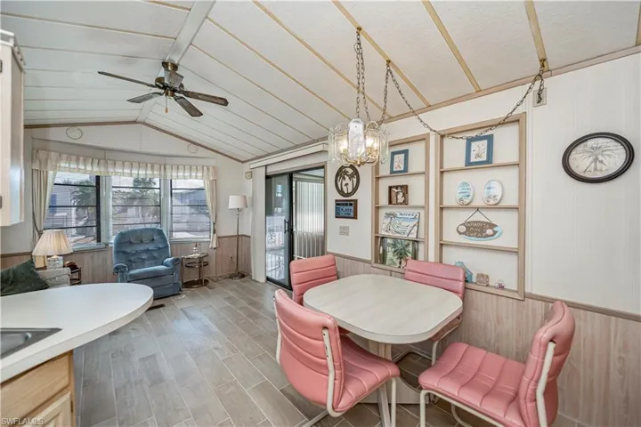 Dining space with wood walls, vaulted ceiling, ceiling fan with notable chandelier, light wood-style flooring, and wainscoting