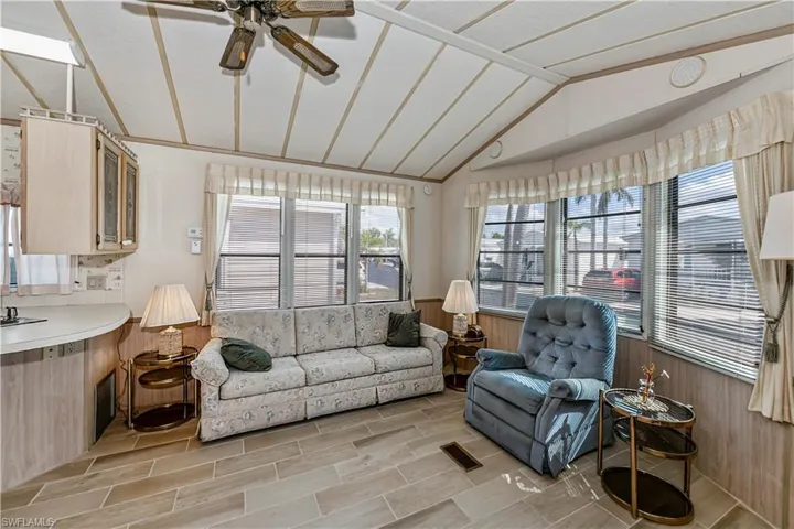 Living area featuring wood walls, vaulted ceiling, a wainscoted wall, visible vents, and a ceiling fan