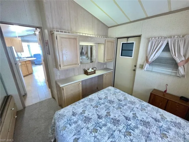 Carpeted bedroom with wallpapered walls, freestanding refrigerator, and vaulted ceiling