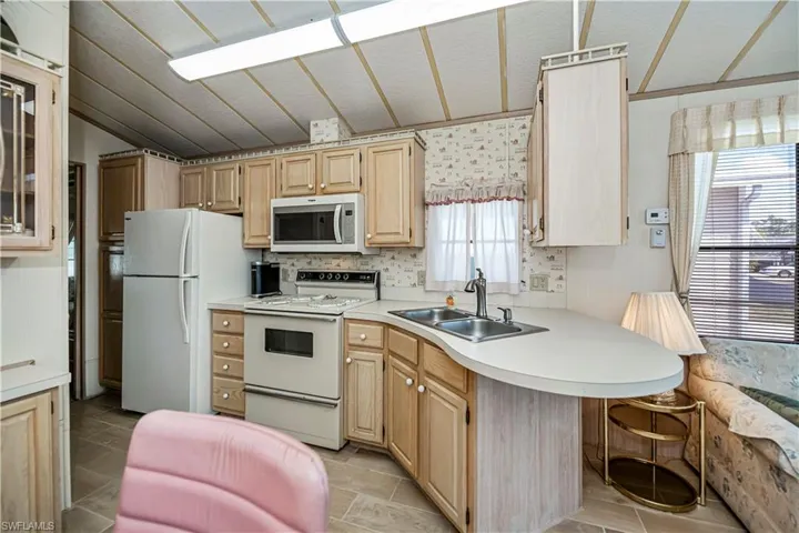 Kitchen with light countertops, white appliances, lofted ceiling, a sink, and light brown cabinetry