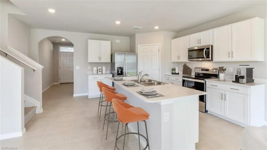 Kitchen featuring stainless steel appliances, white cabinetry, arched walkways, light tile patterned floors, and an island with sink