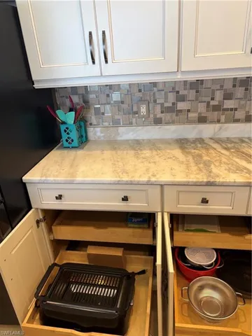 White shaker-style cabinetry with dark hardware, a mosaic tile backsplash, and a light-toned countertop
