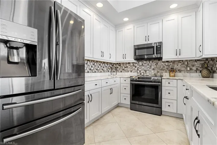Kitchen featuring appliances with stainless steel finishes, white cabinetry, tasteful backsplash, light stone countertops, and light tile patterned flooring