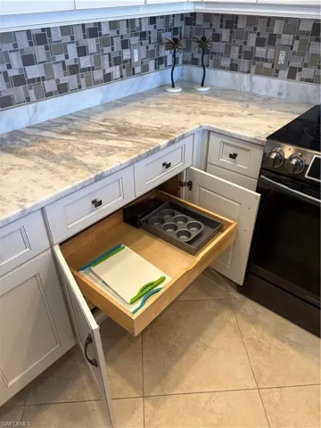 Light-toned cabinetry with dark hardware, stone-finish countertops, mosaic tile backsplash, and tile flooring