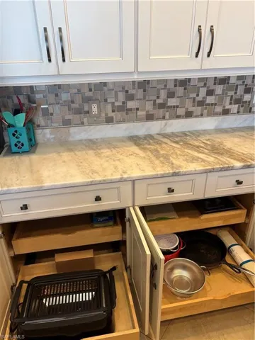 White upper and lower cabinetry with dark hardware, multicolored mosaic tile backsplash, light-toned countertop, and lower pull-out drawers