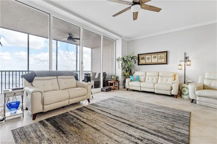 Tiled living room featuring expansive windows, ceiling fan, and ornamental molding