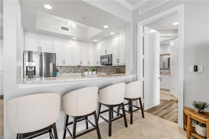 Kitchen with a kitchen bar, backsplash, white cabinets, and stainless steel refrigerator with ice dispenser