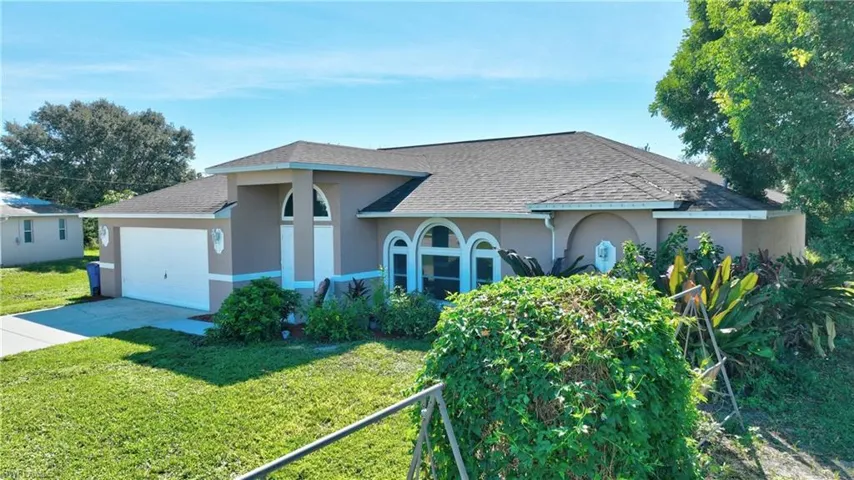 View of front of house with stucco siding, a shingled roof, driveway, and a front yard