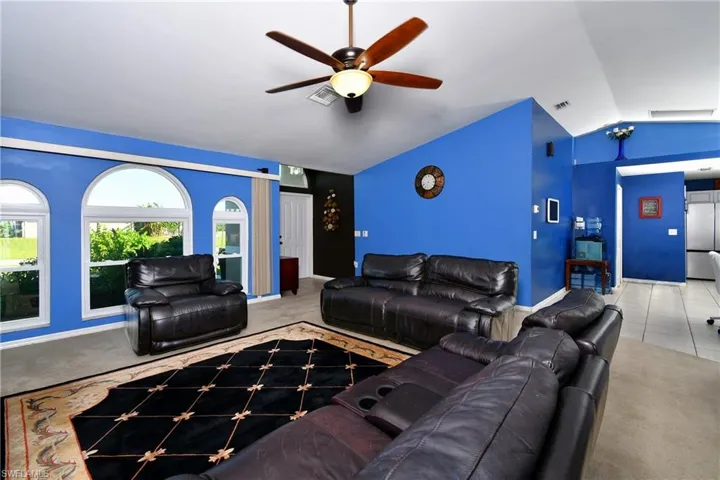 Living room featuring vaulted ceiling, a ceiling fan, light tile patterned flooring, and light colored carpet