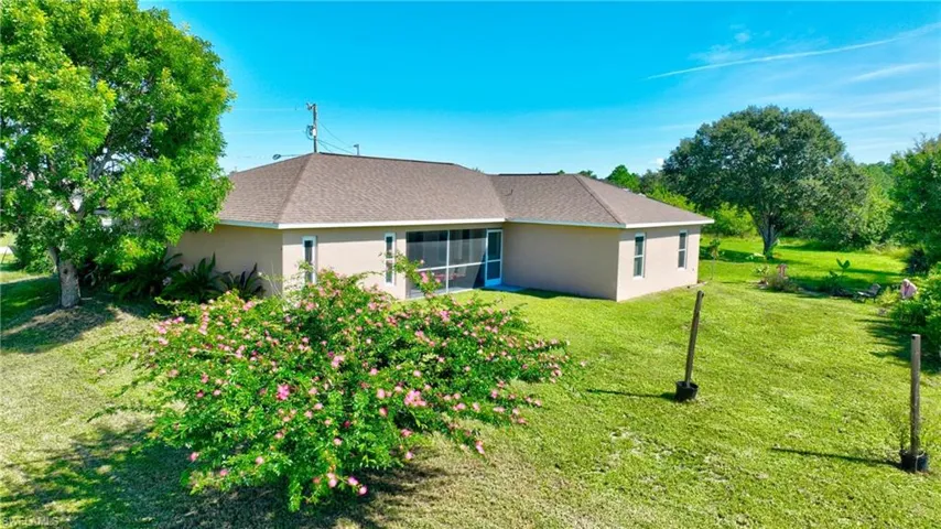 Rear view of house with a yard, stucco siding, and roof with shingles